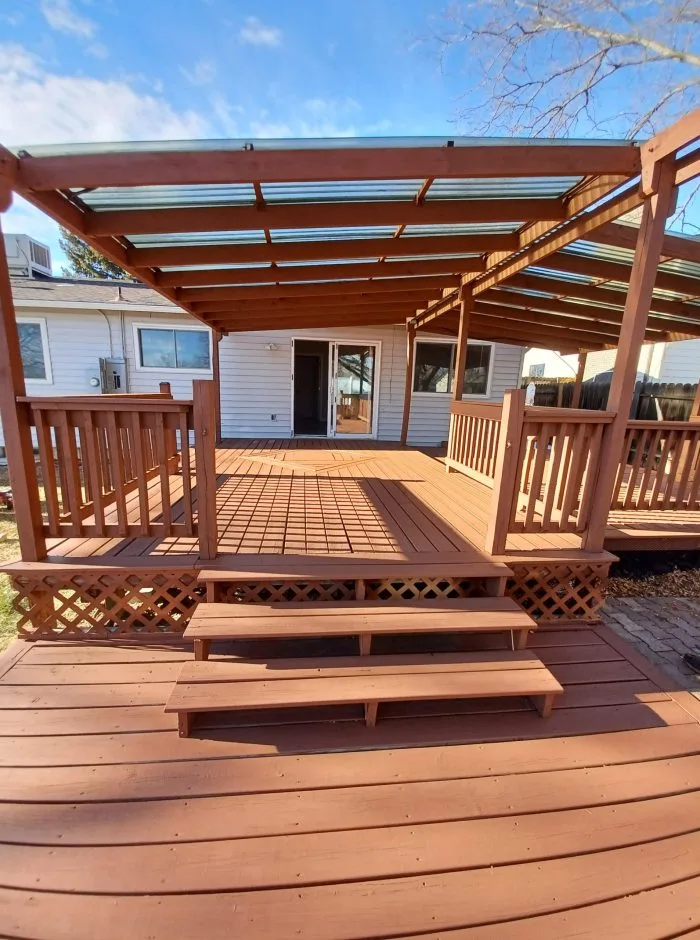 Deck elevado de madera sobre patio trasero junto a la pared lateral de una casa en preparación